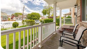 A covered porch with a white railing, outdoor seating, and a view of a residential neighborhood. - Charming Urban3-bedroom  apartment in Hempstead with WiFi and AC (Hempstead)