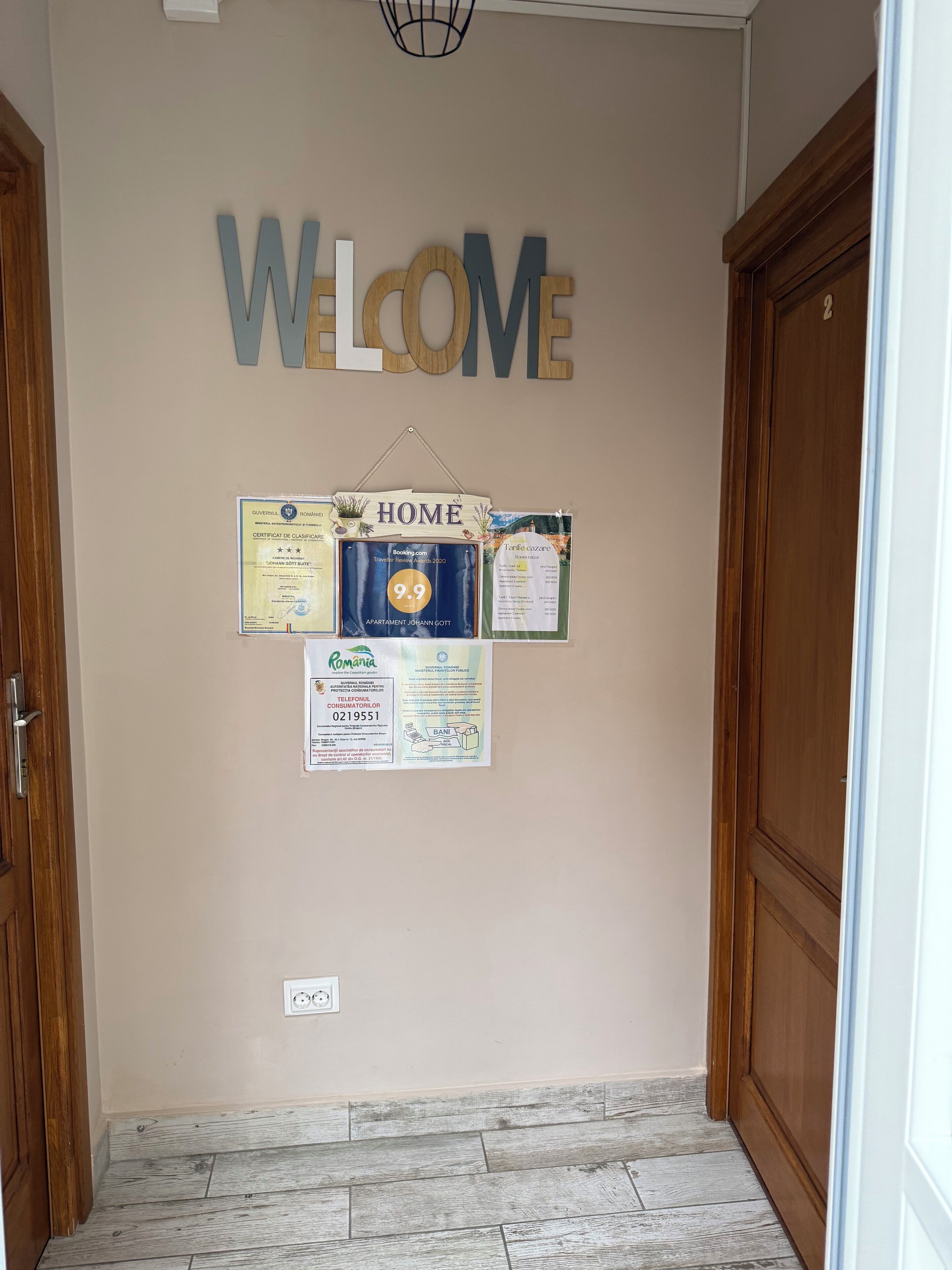 A hallway with a 'WELCOME' sign, a 'HOME' sign, and various notices including a travel award, a bank advertisement, and a consumer protection certificate.
