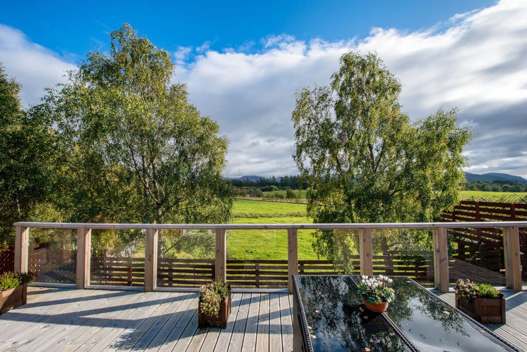 A wooden deck with a glass balustrade overlooking a green landscape.