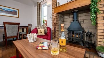 A cozy living room with a fireplace, a wooden table with snacks and a bottle, and a red sofa.