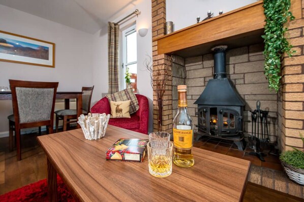 A cozy living room with a fireplace, a wooden table with snacks and a bottle, and a red sofa.