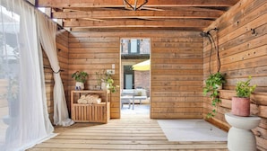 A wooden cabin interior with a wooden floor, a bench, a table, and a doorway leading outside.