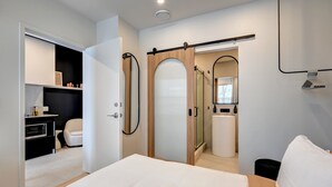 A modern bedroom with a bed, a wardrobe, a bathroom, and a kitchen area.
