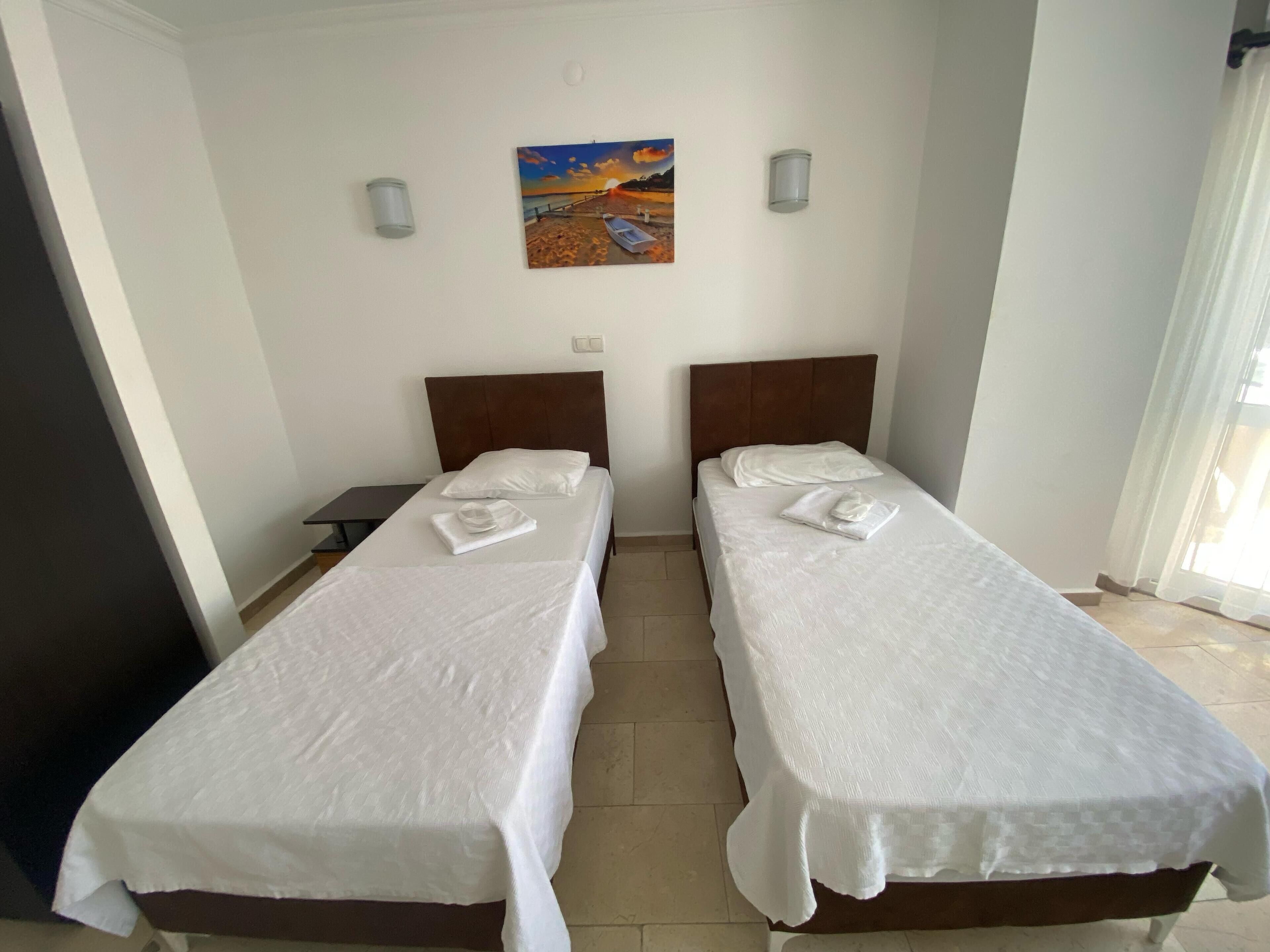 A room with two single beds, a painting on the wall, and a small table.