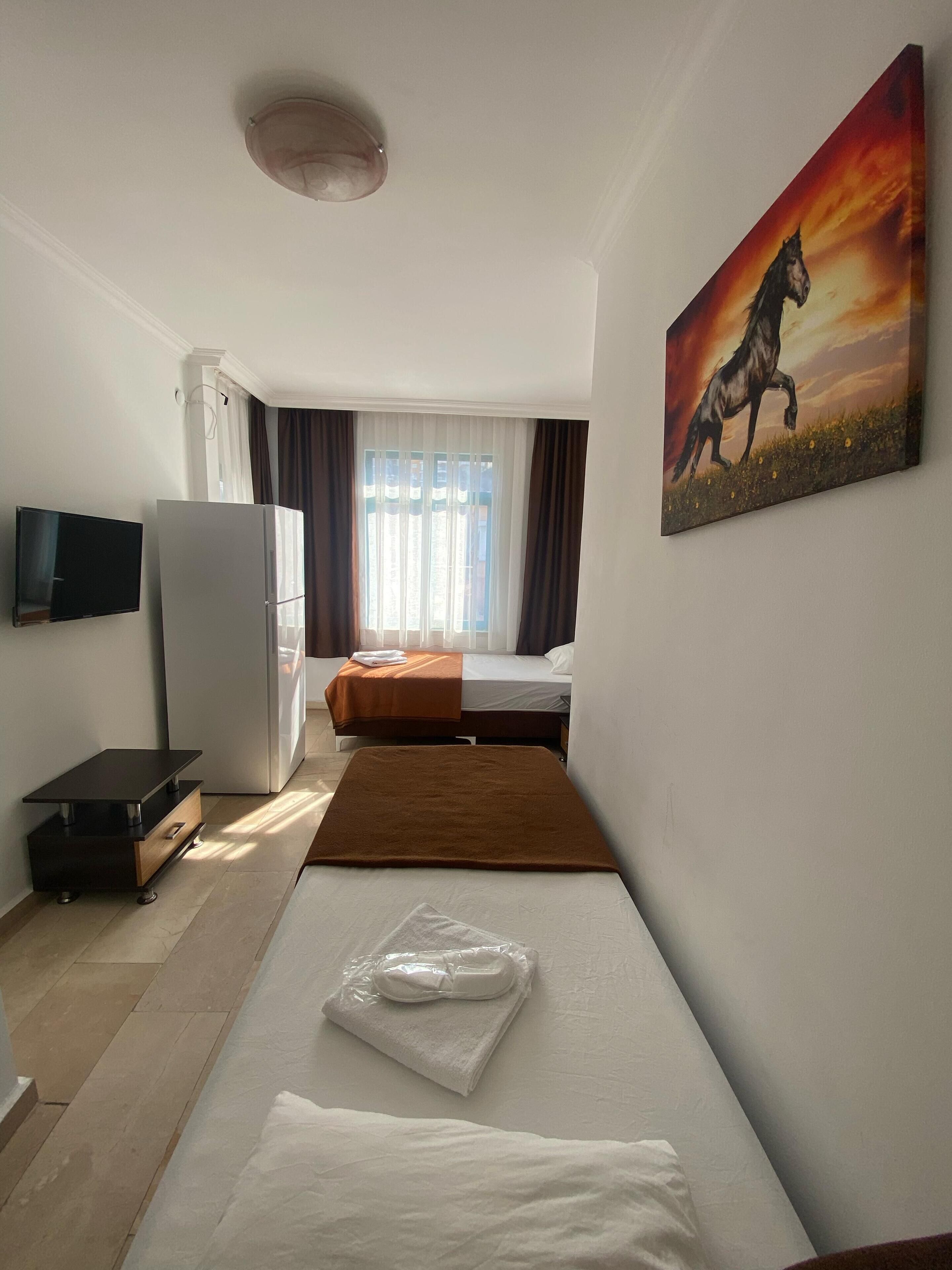 A hotel room with a bed, a desk, a refrigerator, a television, and a painting of a horse.
