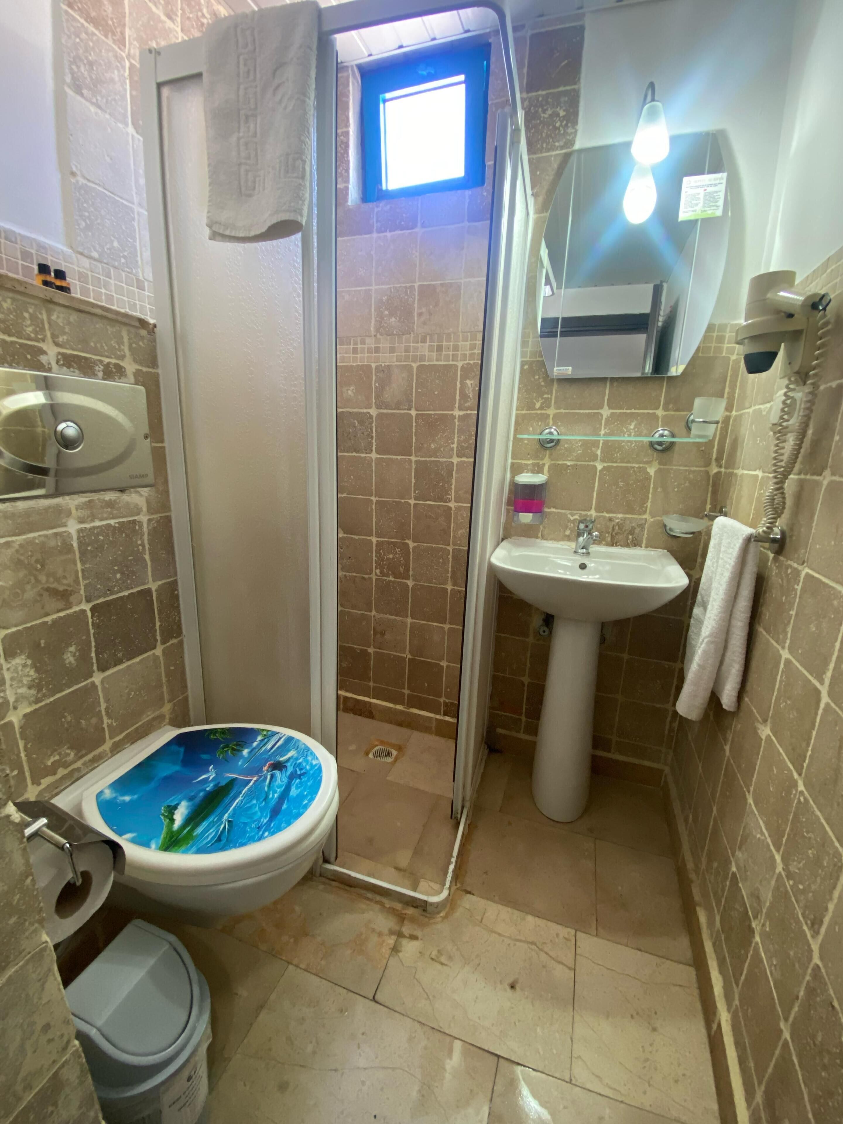 A compact bathroom with a shower, toilet, sink, and a small window.