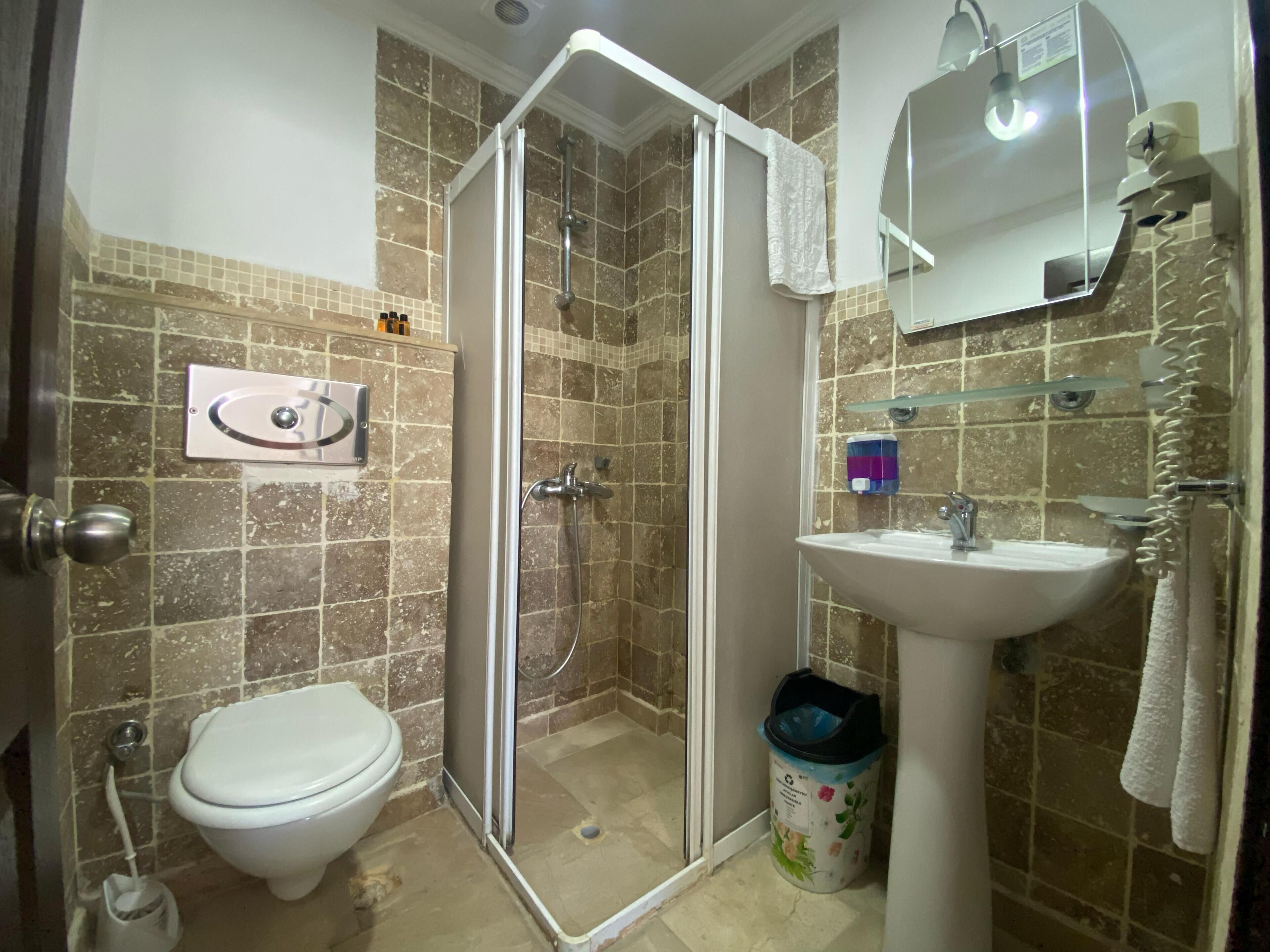 A bathroom with a shower, toilet, sink, and a trash bin.