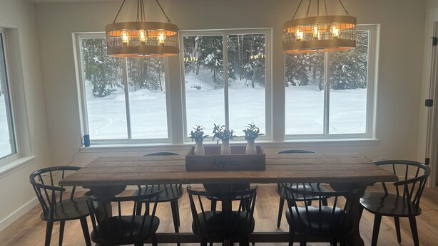 A dining area with a wooden table and black chairs, large windows with a snowy view, and two pendant lights. - Private, luxury, 4-bedroom home minutes from downtown Bigfork (Bigfork)
