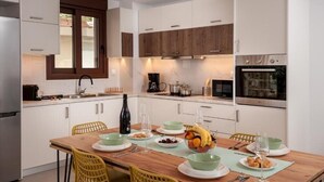 A modern kitchen with white cabinets, wooden accents, a dining table with yellow chairs, and a fruit bowl.