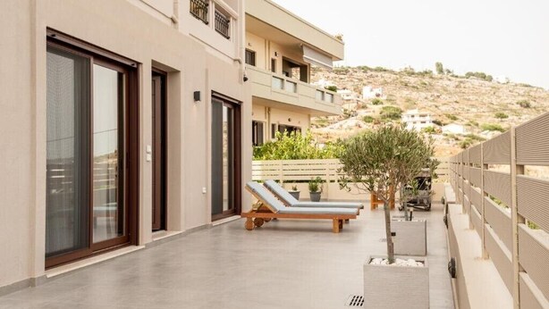 A modern building with a flat roof, large sliding glass doors, and a balcony with sun loungers.