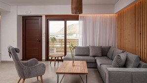 A modern living room with a grey sofa, a grey armchair, and a wooden coffee table. There is a view of a balcony with a wooden wall and a white curtain.