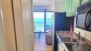 A kitchen with a view to a balcony, wooden flooring, and green cabinets. - Direct Oceanfront and Boardwalk Condo! Decatur House 510 (Ocean City)