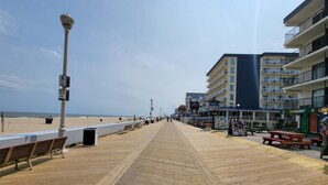 A wooden boardwalk leading to a beach with a row of buildings on the right, including a Subway restaurant. - Direct Oceanfront and Boardwalk Condo! Decatur House 510 (Ocean City)