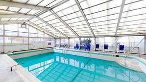 An indoor swimming pool with a glass ceiling, clear water, and blue chairs along the side. - Direct Oceanfront and Boardwalk Condo! Decatur House 510 (Ocean City)