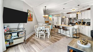 A modern kitchen with white cabinets, a central island, and a dining area with white chairs. - The Beach is Calling-this 3bd Villa is the answer! (Hilton Head Island)