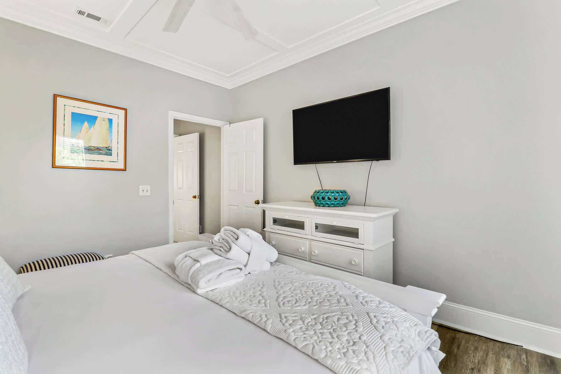 A hotel room with a bed, a TV mounted on the wall, a white dresser, and a framed picture on the wall.