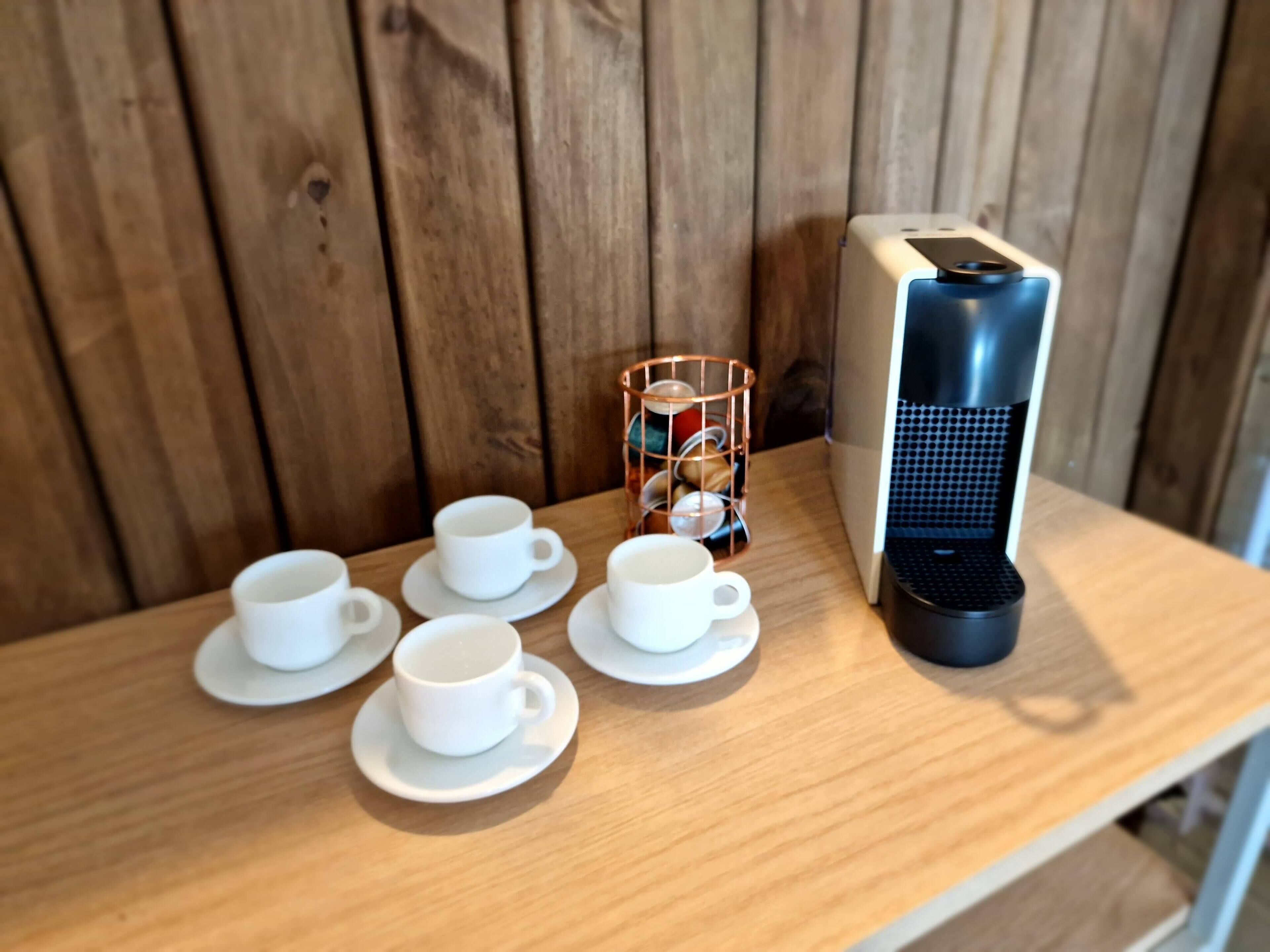 A wooden table with six white cups and saucers, a coffee maker, and a copper mug rack.