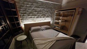 A bedroom with a brick-patterned wall, a bed with a white bedspread, a bedside table, and a wardrobe with shelves. - CalaRosa . Condomínio (Imbituba)