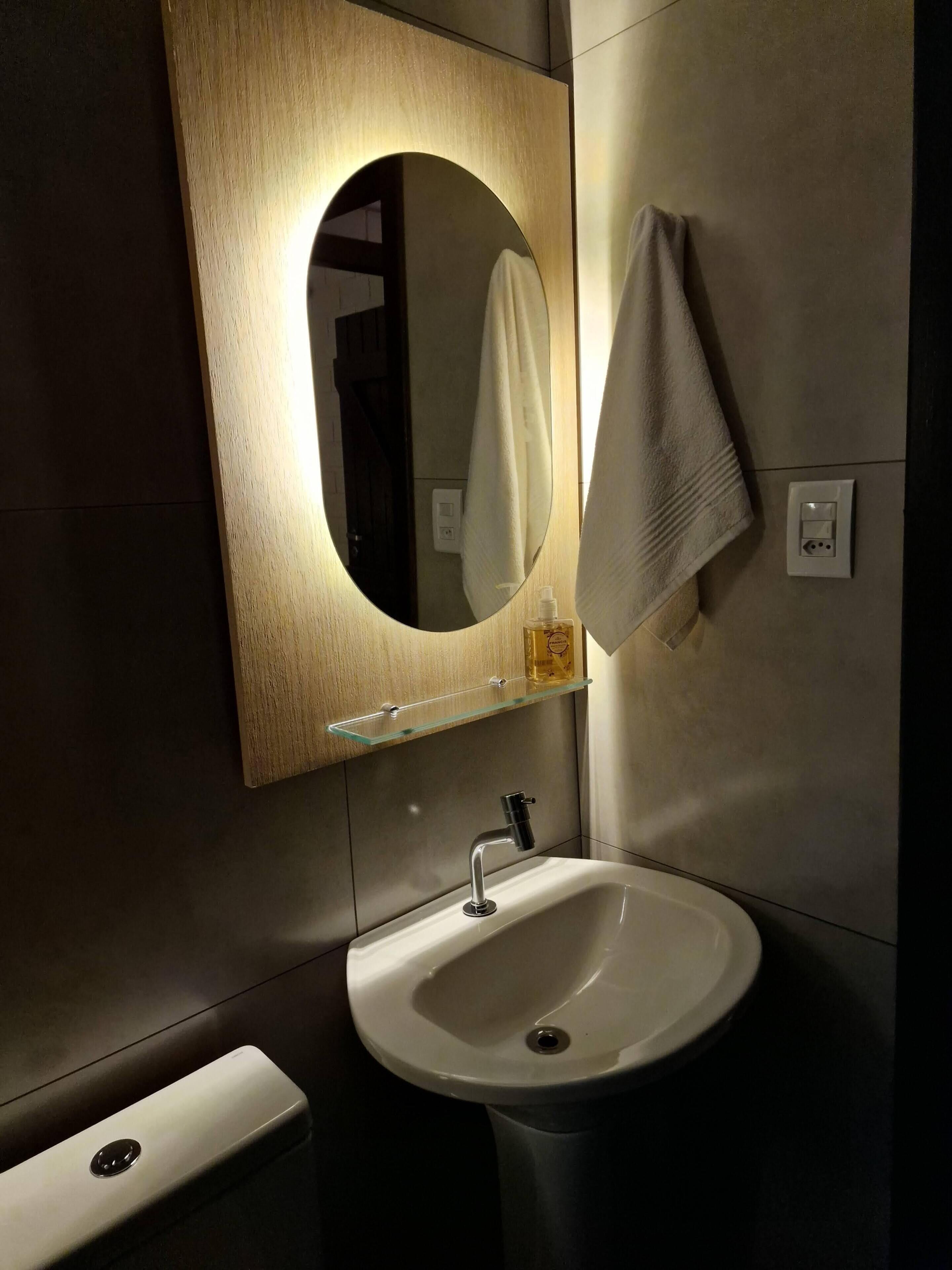 A modern bathroom with a white sink, a round mirror with a wooden frame, and a towel hanging on the wall.