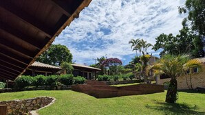 A courtyard with a stone wall, a wooden staircase, and a covered area with a tiled roof. - CalaRosa . Condomínio (Imbituba)