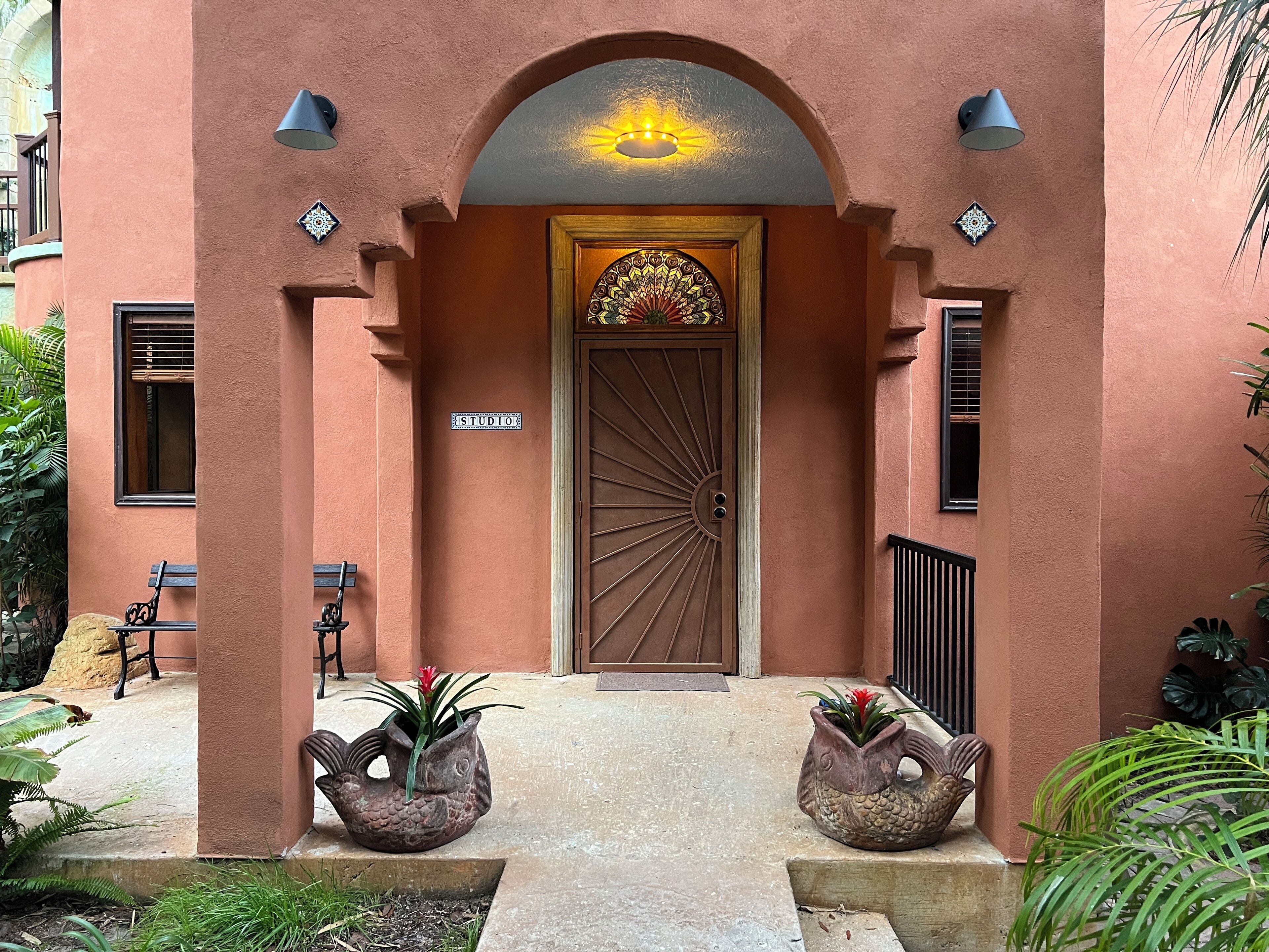 A building entrance with a 'STUDIO' sign, a decorative door, and two bird-shaped planters.