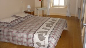 Un dormitorio con una cama grande, una mesita de noche, una pequeña mesa, una ventana con cortinas y un jarrón con flores.