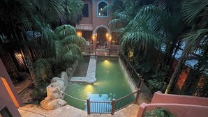 Un espace piscine agrémenté d’un petit pont, entouré de palmiers et bordé d’un bâtiment surmonté d’un dôme.