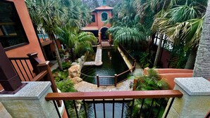 Une cour agrémentée d’un él ément décoratif aquatique, entourée de palmiers et bordée d’un bâtiment au toit rouge.