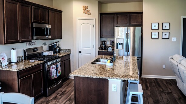 A kitchen with dark wood cabinets, granite countertops, stainless steel appliances, and a white door. - Houma Way From Home with Arcade & EV Charger (Houma)