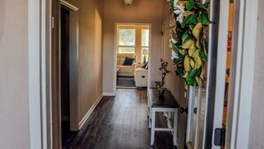 A hallway with a dark wooden floor, a white bench, and a door on the left. - Houma Way From Home with Arcade & EV Charger (Houma)