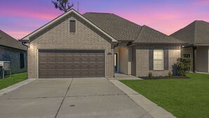 A two-story house with a brick facade, a large garage, and a well-maintained lawn. - Houma Way From Home with Arcade & EV Charger (Houma)