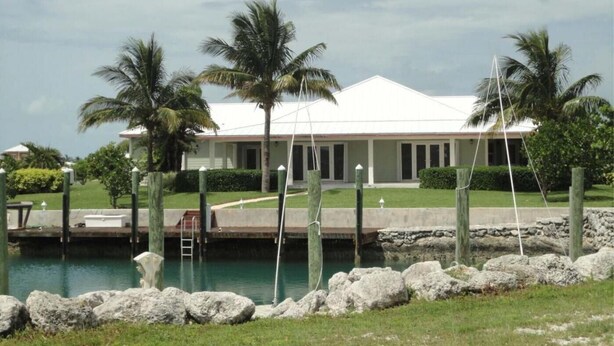 A beachfront property with a pool, palm trees, and a white building. - Charming 3-bedroom house with WiFi, Dockage, AC in West End (West End)