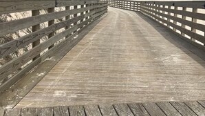 Une promenade en bois menant à une plage, avec un ciel dégagé.