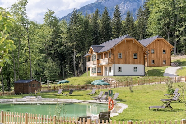 A wooden lodge with a pool, surrounded by a wooden fence and trees.