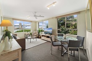 A modern living room with a glass table, chairs, a sofa, a TV, and a ceiling fan.