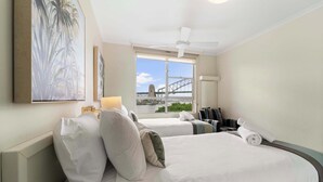 Une chambre d’hôtel avec deux lits, un ventilateur de plafond, une grande fenêtre donnant sur un pont et des œuvres d’art accrochées au mur.