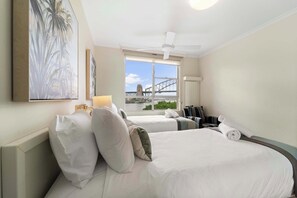 A hotel room with two beds, a ceiling fan, a large window with a view of a bridge, and artwork on the wall.