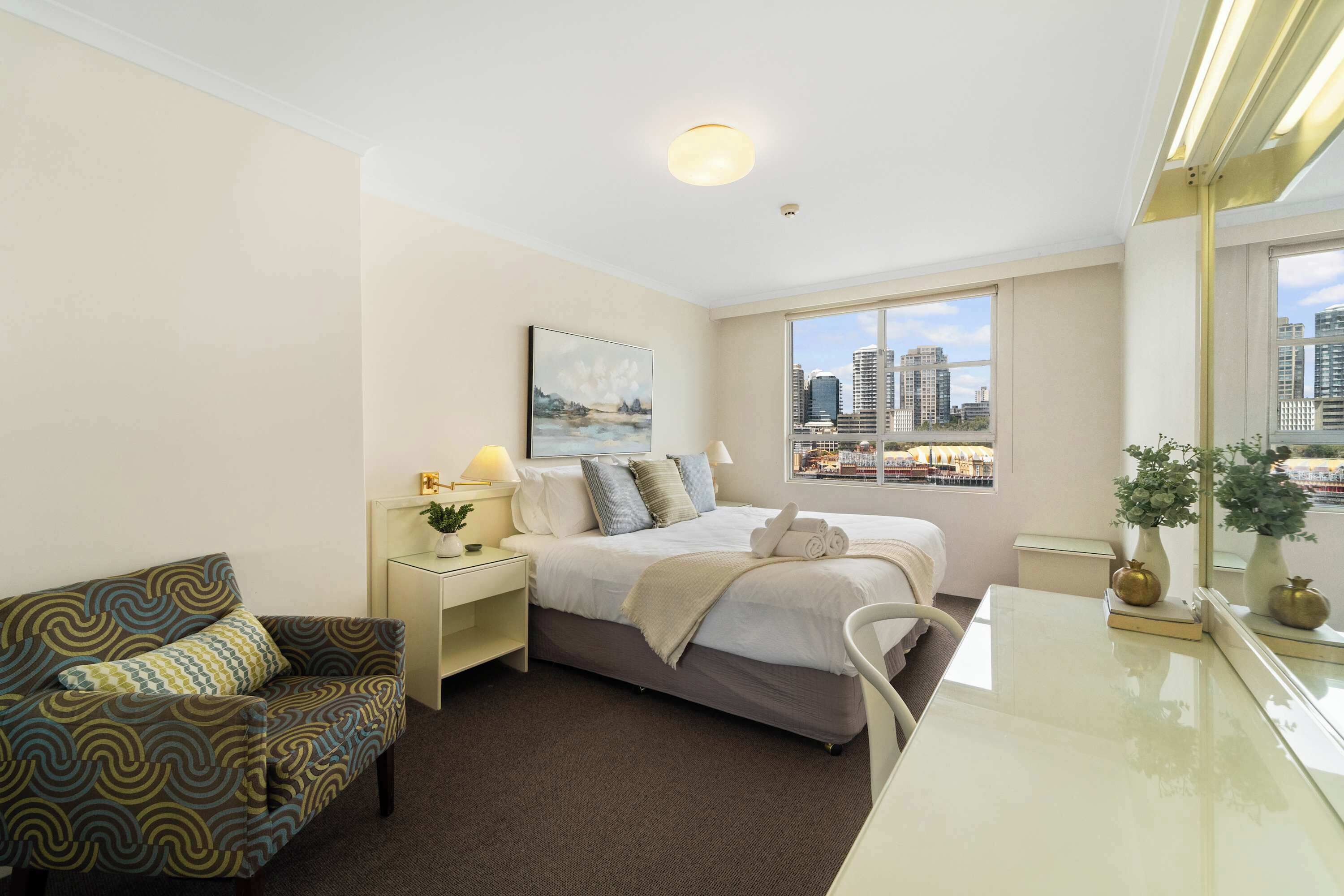 A hotel room with a bed, a sofa, a desk, and a view of the cityscape.