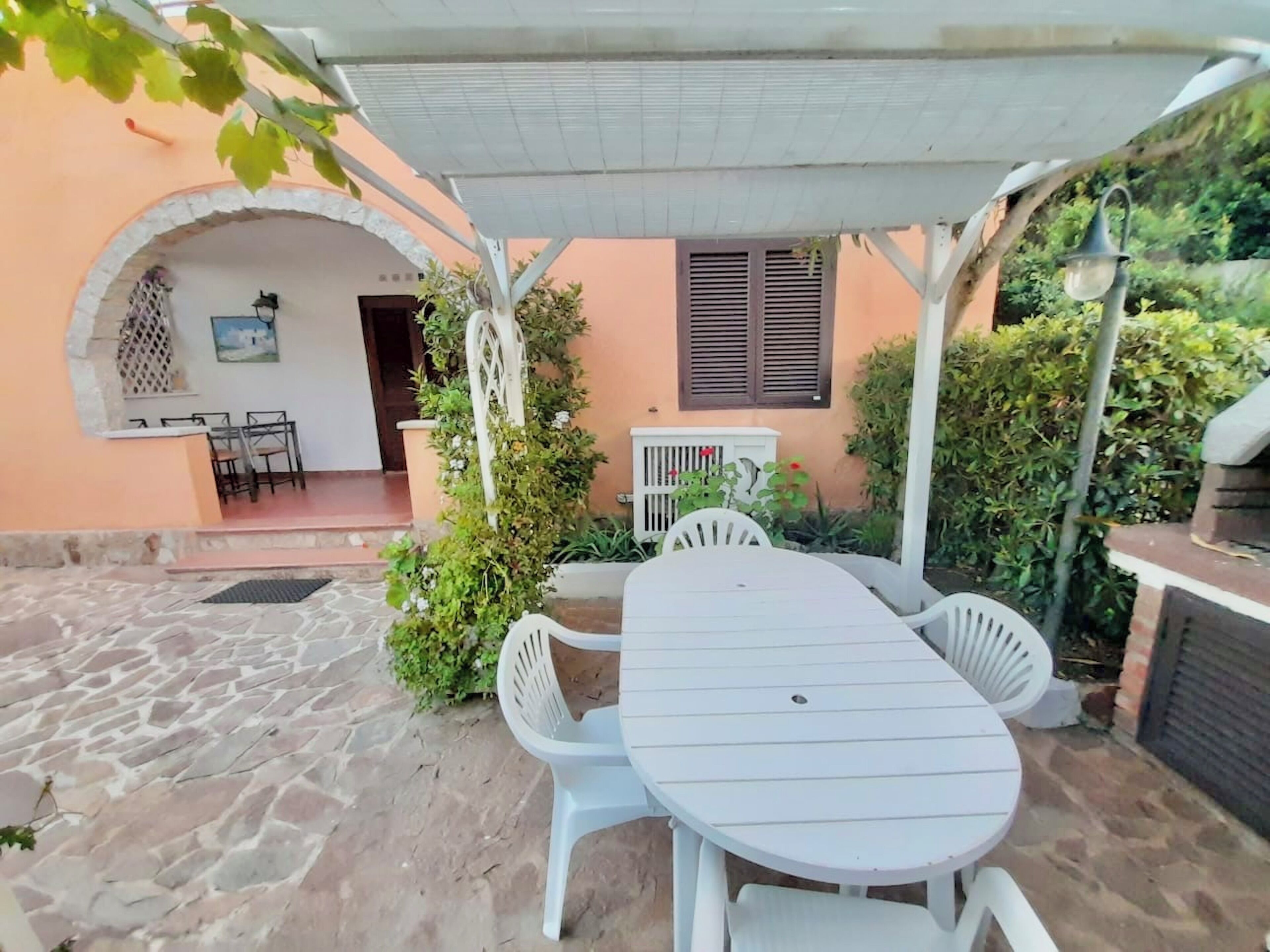 Une terrasse avec une table et des chaises blanches, un espace abrité et un sol en pierre.