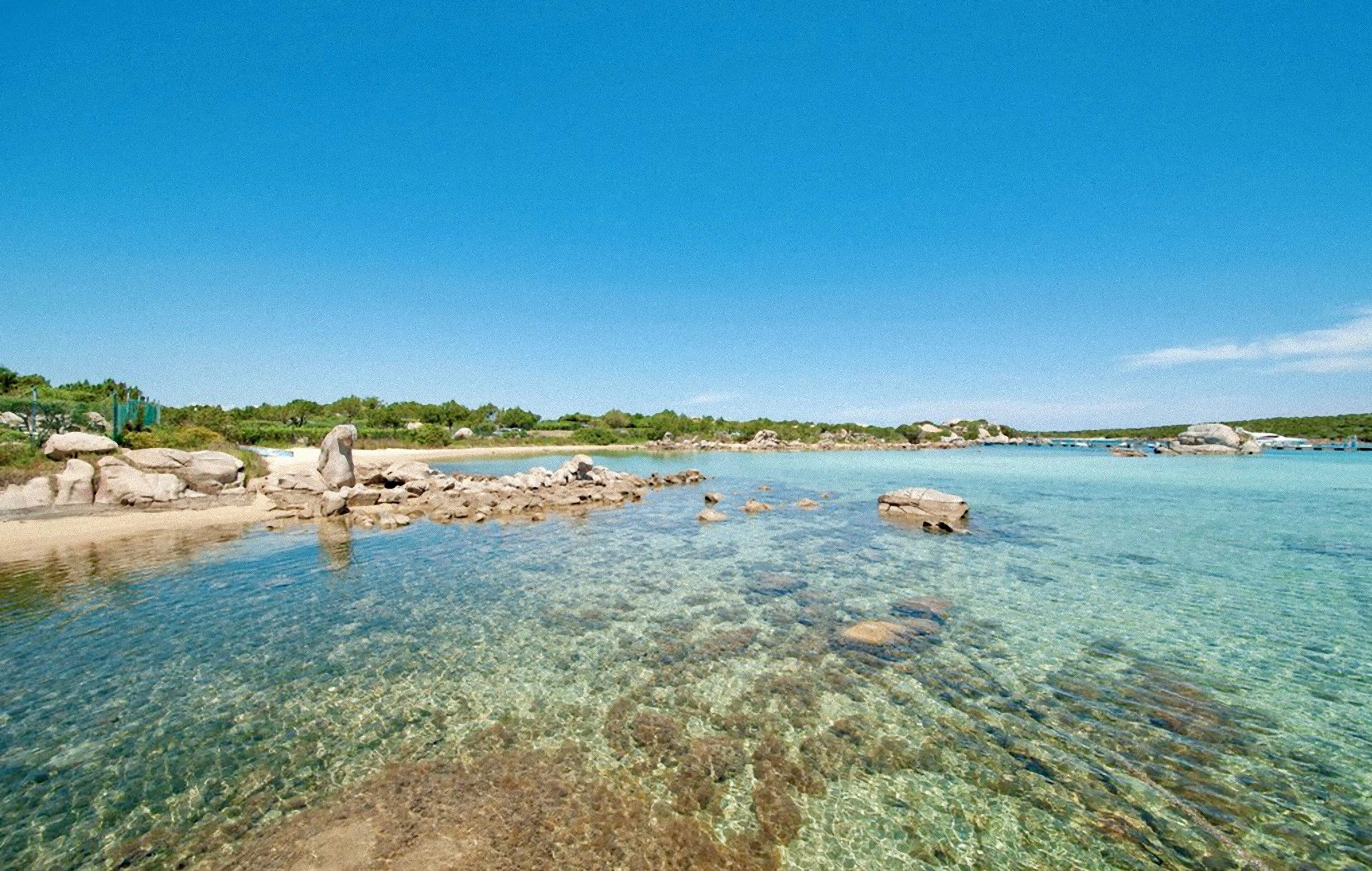 A clear coastal beach with visible rocks and calm waters.