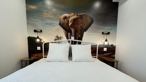 A bedroom with a large bed, a mural of an elephant, and two bedside tables with lamps. - Parifou Air-conditioned cosy house with play area for families (Riom)