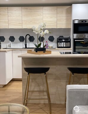 A modern kitchen with a central island, bar stools, a sink, and a built-in oven. - Parifou Air-conditioned cosy house with play area for families (Riom)