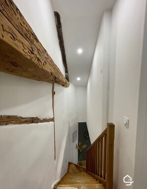 A narrow staircase with wooden steps and a wooden handrail, leading to a landing with a white wall and a framed picture. - Parifou Air-conditioned cosy house with play area for families (Riom)