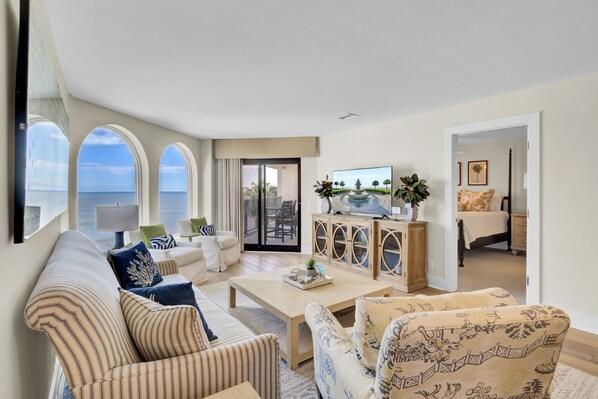 Un salon spacieux avec une grande fenêtre donnant sur la mer, un canapé confortable, une table basse et un téléviseur posé sur un meuble en bois.