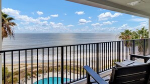 Een balkon met uitzicht op de oceaan, een zwembad en palmbomen.