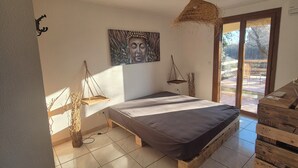 Un dormitorio con una cama, un cuadro de Buda, una lámpara colgante y vistas a través de un ventanal.