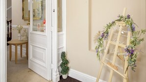 A hotel reception area with a wooden desk, a small potted plant, and a decorative easel with a floral arrangement. - Hotel Sofia (Blackpool)