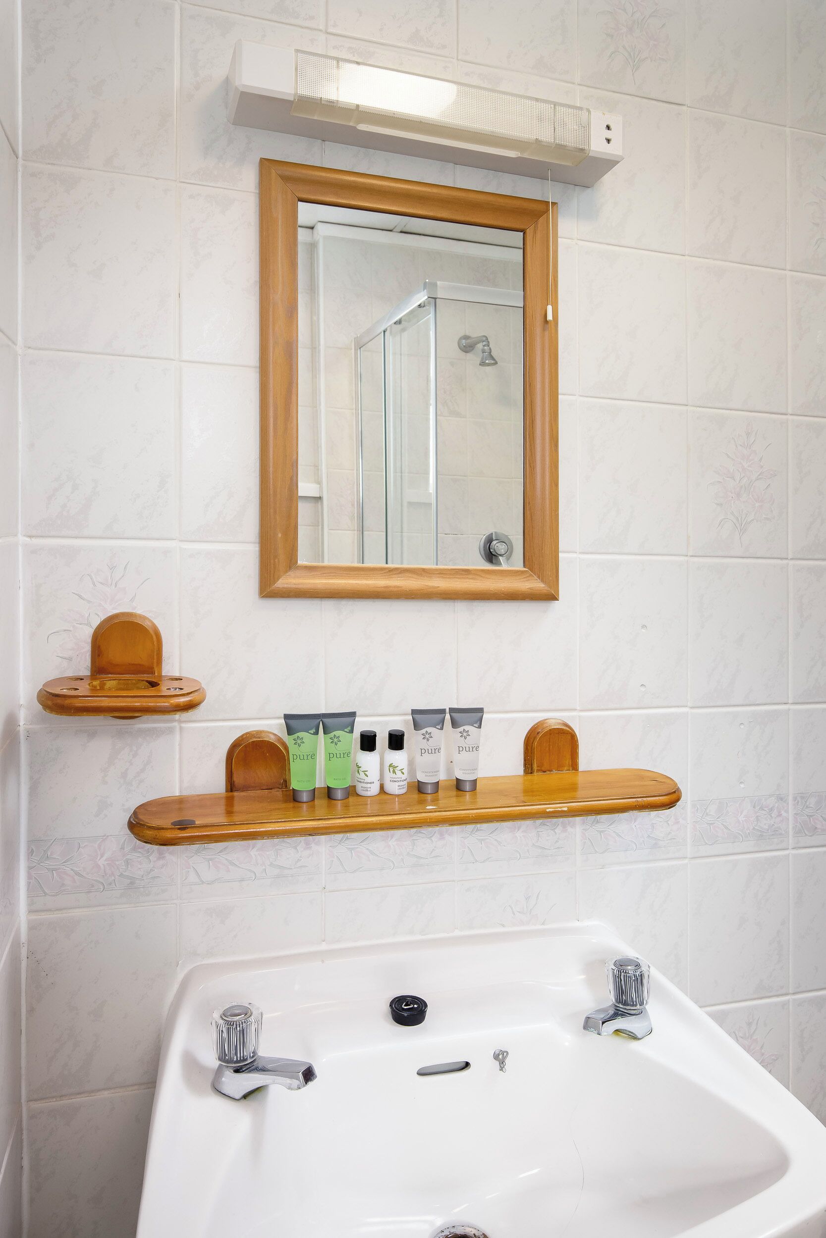 Une salle de bain avec un lavabo blanc, un miroir avec un cadre en bois et une étagère contenant des articles de toilette.
