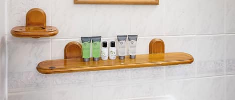 Une salle de bain avec un lavabo blanc, un miroir avec un cadre en bois et une étagère contenant des articles de toilette.