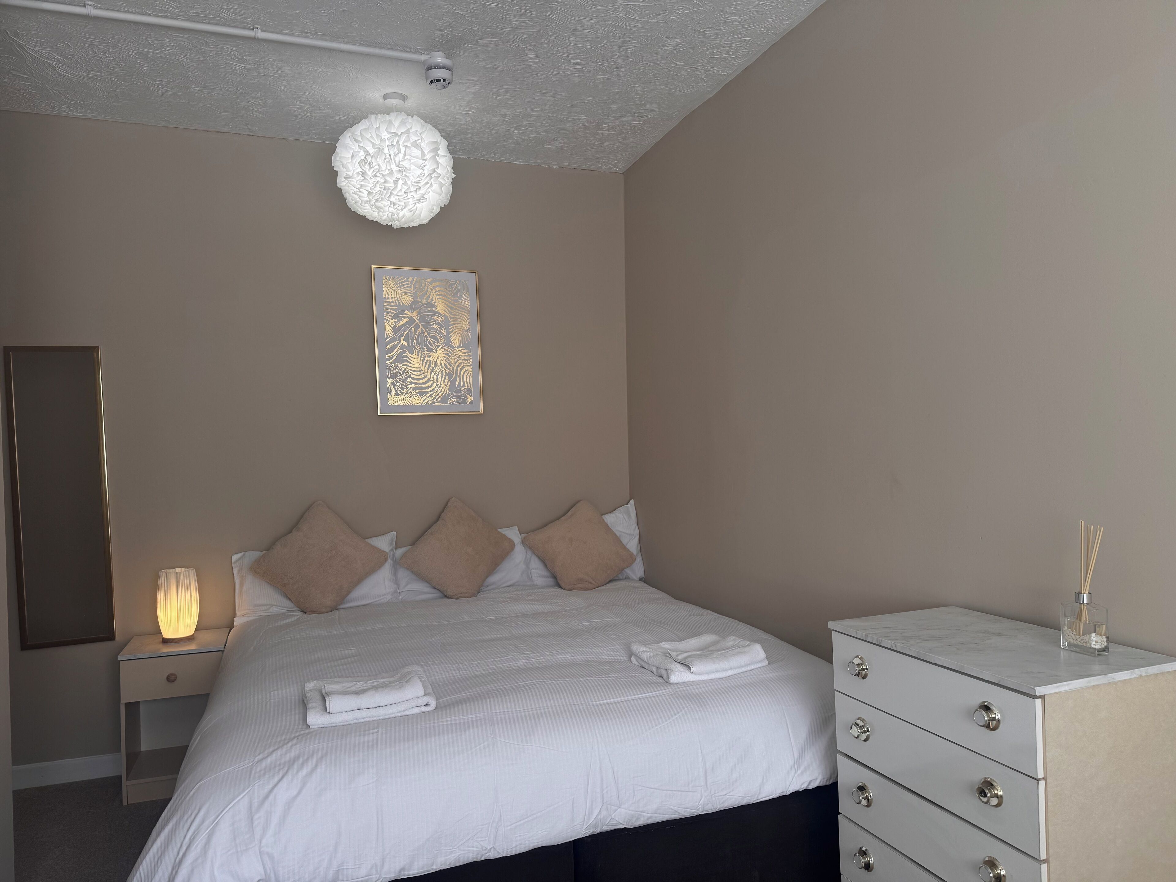 Un dormitorio ordenado con cama, lámpara de noche y cómoda.